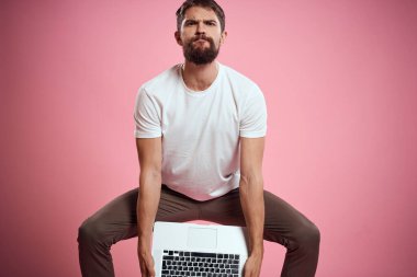 Açık dizüstü bilgisayarı olan beyaz tişörtlü bir adam elleri kırpılmış yeni teknoloji klavye monitörüyle jest yapıyor.