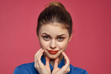 Parlak makyajlı, pembe arka plan hareketleriyle mavi gömlekli enerjik bir kadın.