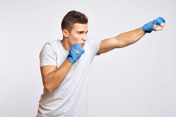 Boxeador masculino deportivo con guantes azules practicando golpes sobre un fondo claro recortado vista — Foto de Stock