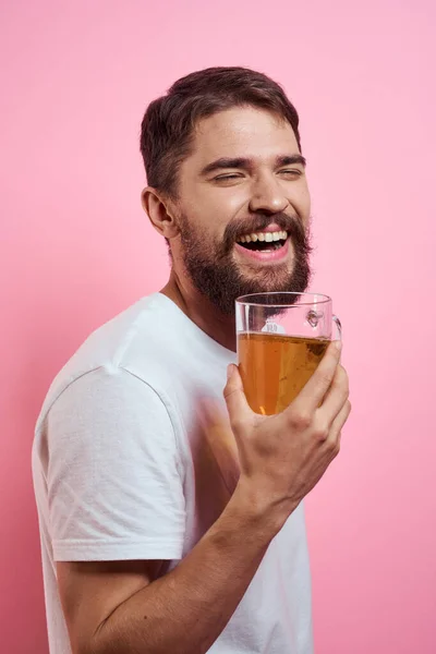 Hombre barbudo con una taza de cerveza En un fondo rosa emociones divertidas recortado vista de una camiseta blanca borracho — Foto de Stock