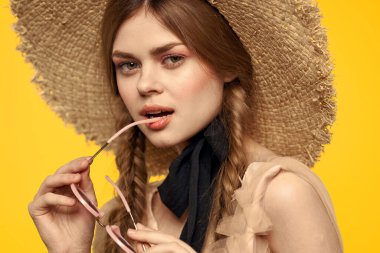Şapkalı romantik bir kadın sarı arka planda eğleniyor ve güneş gözlüğü siyah kurdele modeli portresi takıyor.