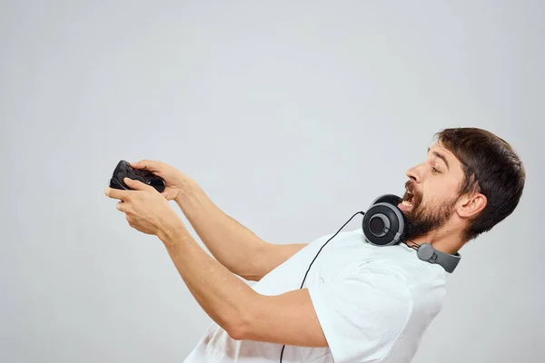 Homem com fones de ouvido gamepad jogando lazer tecnologia branco t-shirt luz fundo — Fotografia de Stock