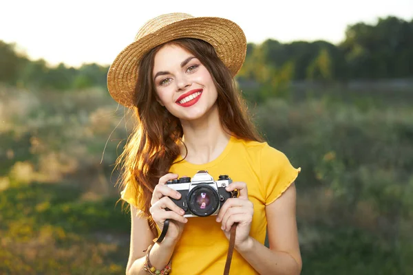 Wanita tersenyum di topi dengan kamera di tangan kuning t-shirt alam — Stok Foto