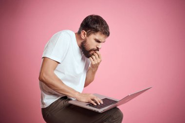 Açık dizüstü bilgisayarı olan beyaz tişörtlü bir adam elleri kırpılmış yeni teknoloji klavye monitörüyle jest yapıyor.