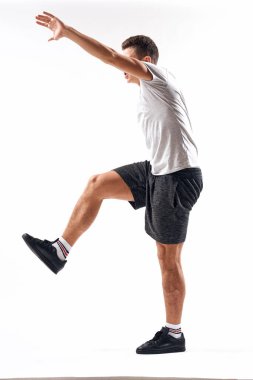Hafif bir geçmişi olan atletik bir adam tam boy ve koşu şortu spor ayakkabısı tişörtü giyiyor.