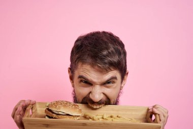 Elinde tepsi olan agresif bir adam. Hamburger kızartması. Pembe arka plan.