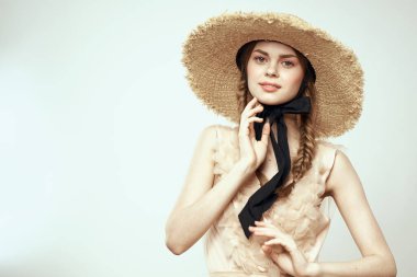 Hasır şapkalı, siyah kurdeleli ve arka planda açık bir elbise giyen hoş bir kız. Romantik bir model.