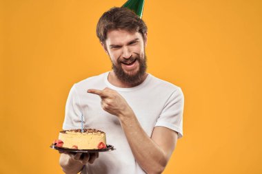 Sakallı ve şapkalı yakışıklı bir adam doğum günü partisi sarı arka planını kutluyor.