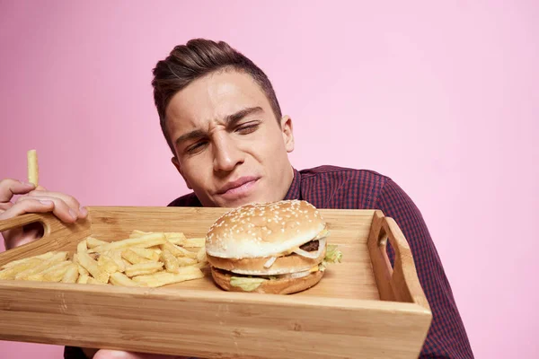 ファーストフードのある男食べるハンバーガーフライドポテトピンクの背景 — ストック写真