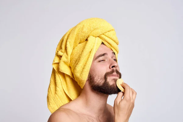 Homem com uma toalha amarela em sua cabeça ombros nus esponja pele limpa cuidados faciais luz fundo — Fotografia de Stock