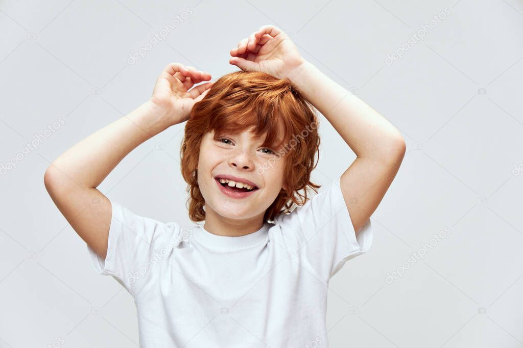Cute red-haired boy holding hands on his head smile white t-shirt childhood