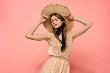 Pembe arka planda siyah kurdeleli şık elbiseli ve şapkalı bir kadın model duygularının eğlenceli görüntüsünü kırptı.