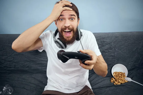 Man sitting on sofa wearing headphones with gamepad playing food leisure technology lifestyle — Stock Photo, Image