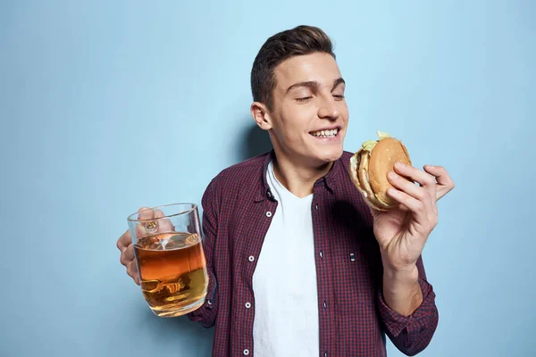 Homme ivre gai avec tasse de bière et hamburger à la main régime alimentaire mode de vie bleu fond — Photo