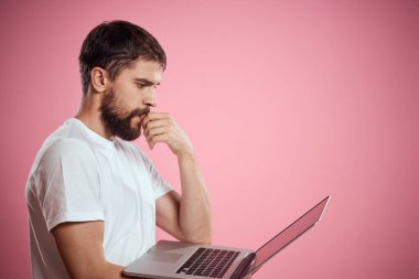 Açık dizüstü bilgisayarı olan beyaz tişörtlü bir adam elleri kırpılmış yeni teknoloji klavye monitörüyle jest yapıyor.