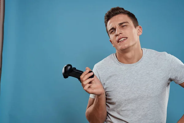 Un hombre con un joystick en sus manos entretenimiento tecnología de ocio videojuegos fondo azul camiseta blanca —  Fotos de Stock