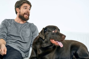 Beyaz bir kanepede siyah köpeği olan bir adam. Arka planda, yakın planda kesilen evcil hayvan insan arkadaş duyguları. Eğlenceli.