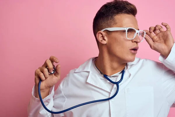 Médecin masculin en robe médicale avec un stéthoscope autour du cou sur un fond rose et des lunettes sur le visage — Photo