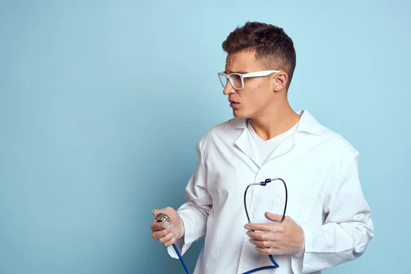 Pracownik medyczny w szlafroku i okularach trzyma stetoskop w dłoniach na niebieskim tle przycięty widok — Zdjęcie stockowe
