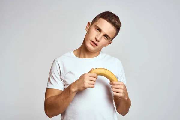 Man met een banaan in zijn hand op een lichte achtergrond leuke emoties licht achtergrond wit t-shirt model — Stockfoto
