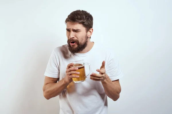 Homme avec une tasse de bière dans ses mains et un t-shirt blanc fond clair moustache barbe émotions modèle — Photo