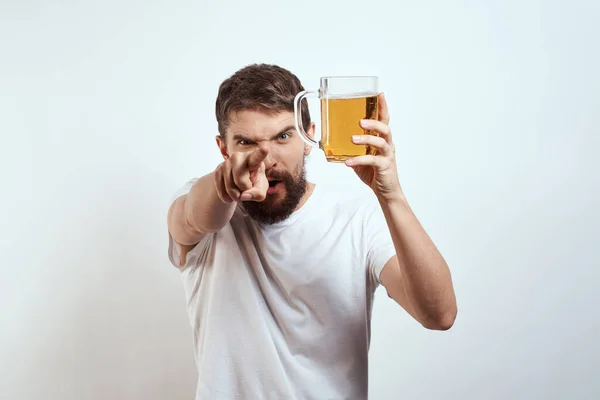 Man med en mugg öl i händerna och en vit t-shirt ljus bakgrund mustasch skägg känslor modell — Stockfoto