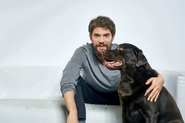 Erkek sahibi kanepede köpekle oynuyor. Eğlenceli ışık odası arkadaşları evcil hayvanı eğitiyor.