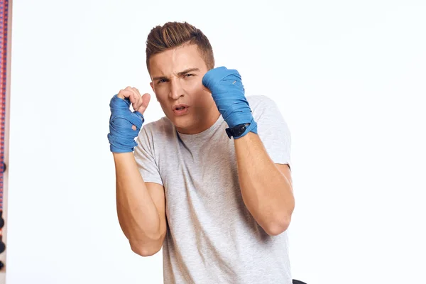 Sportovní mužský boxer v modrých rukavicích cvičení údery na světlém pozadí oříznutý pohled — Stock fotografie