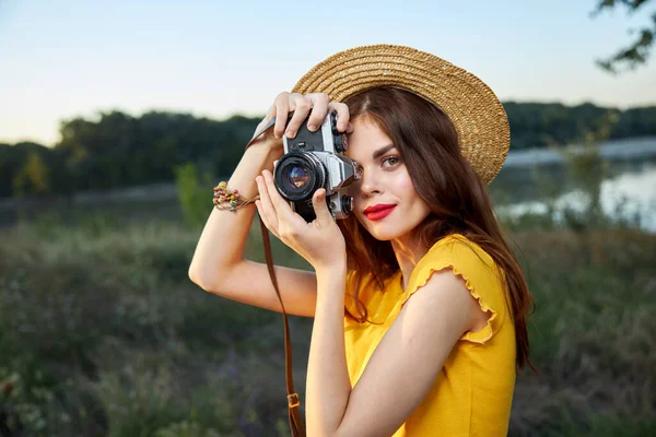 Woman holding camera looks into the camera lens red lips hat nature fresh air lifestyle