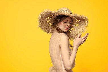 Sarı arka planda saman şapkalı portre kadın. Yazlık elbise mankeni romantizmi.