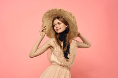 Pembe arka planda siyah kurdeleli şık elbiseli ve şapkalı bir kadın model duygularının eğlenceli görüntüsünü kırptı.