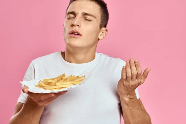 Hombre con papas fritas en una caja de papel sobre un fondo rosa calorías comida rápida retrato rosa fondo — Foto de Stock