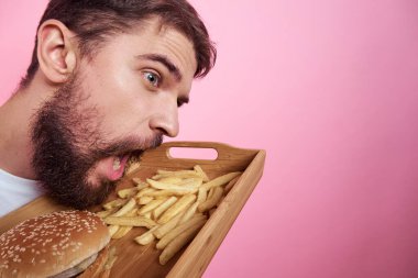 Elinde yemek tepsisi olan bir adam hamburger kızartması ve fast food kalorisi pembe arka plan portresi.