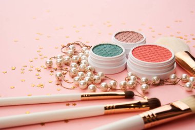 Göz falı aksesuarlar, boncuklar makyaj fırçaları pembe arka planda profesyonel kozmetik ürünleri koleksiyonu.