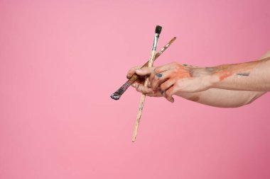 Elleri fırçalı bir adam pembe arka plan hobisi yaratıcı yaklaşımı boyuyor.