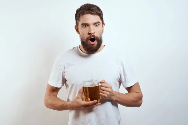 Homme avec une tasse de bière dans ses mains et un t-shirt blanc fond clair moustache barbe émotions modèle — Photo