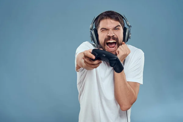 Hombre en auriculares controlador en las manos jugando consola estilo de vida emociones azul fondo blanco camiseta —  Fotos de Stock