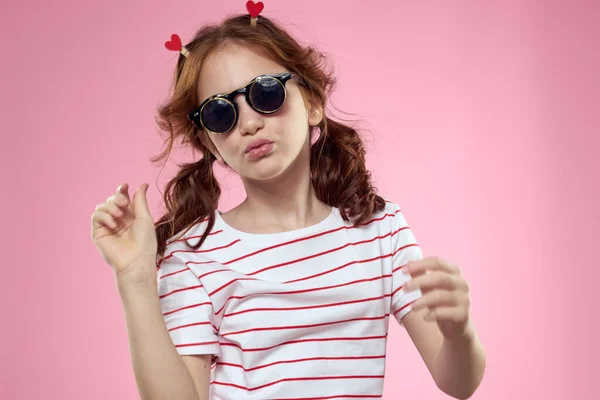 Aranyos lány napszemüveg csíkos t-shirt életmód szórakoztató stílus rózsaszín háttér — Stock Fotó
