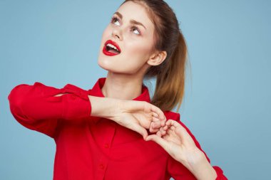 Parlak elbiseli bir kız, elleri mavi arka planda kırpılmış bir kalp gösterir.