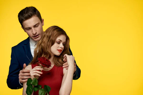 Amoureux homme et femme avec une rose rouge dans leurs mains étreignant sur un fond jaune romance relation amour famille — Photo