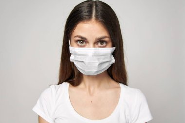 Tıbbi maske takan kadın öne doğru beyaz tişört giyiyor. 