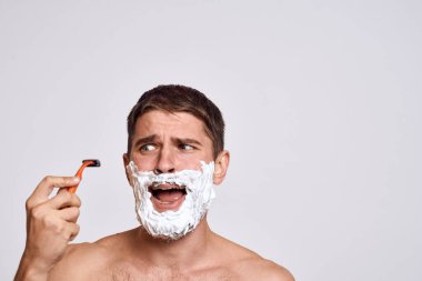 Yüzünde beyaz tıraş köpüğü olan yakışıklı bir adam ve jilet gibi omuzları olan temiz bir cilt.