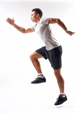 Spor şortlu bir sporcu ve arka planda bir tişört var ve tam gelişim göstererek kenarda koşuyor.