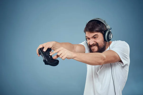 Hombre en auriculares controlador en las manos jugando consola estilo de vida emociones azul fondo blanco camiseta —  Fotos de Stock
