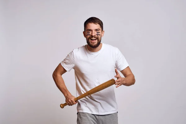 Un uomo emotivo con una mazza da baseball su uno sfondo chiaro in una t-shirt bianca sta gesticolando con le mani al modello — Foto Stock