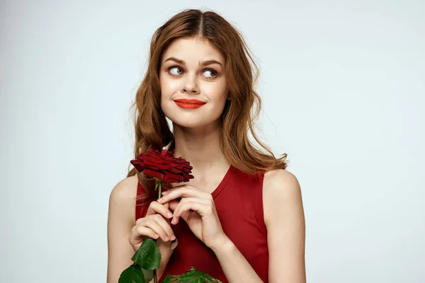 Gyönyörű nő piros ruhában tart egy rózsát a kezében egy ajándék virágok dekoráció vonzó megjelenés — Stock Fotó