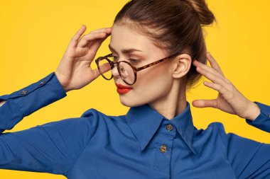 Mavi gömlekli, gözlüklü, yüzünde parlak makyajlı bir kadın elleriyle işaret ediyor.