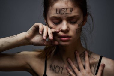 Hüsrana uğramış bir kadın vücudunda çirkin yazıtlar ve gri bir arka plan portresi üzerinde siyah bir tişört var. 