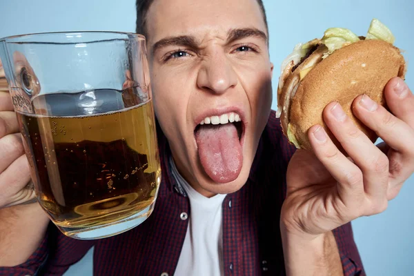 Homme ivre gai avec tasse de bière et hamburger à la main régime alimentaire mode de vie bleu fond — Photo