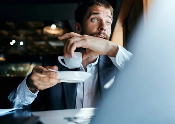 Homme d'affaires assis dans un café avec une tasse de café dans ses mains devant un ordinateur portable communication technologique — Photo